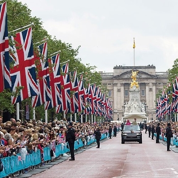 large crowds line the mall which is decorated with flags and Buckingham Palace can be seen in the background