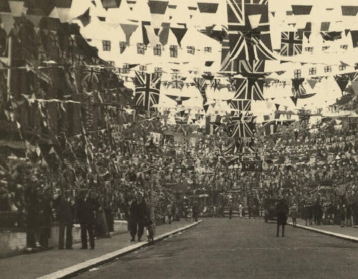 Black and white photo showing a street decorated with large amounts of flags and bunting