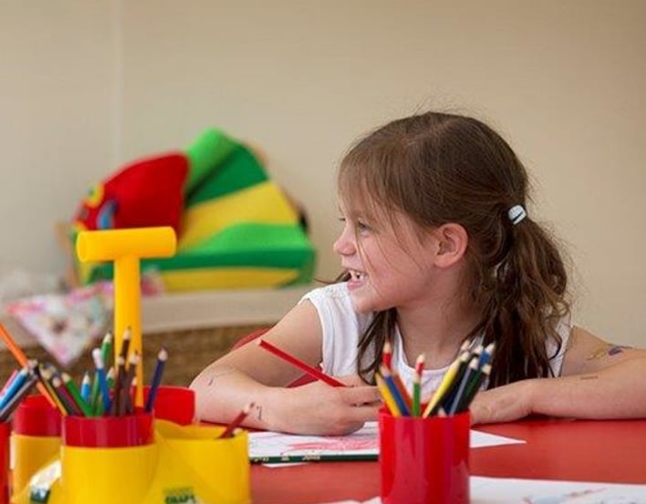 A girl smiling with a pot of colouring in pencils in front of her