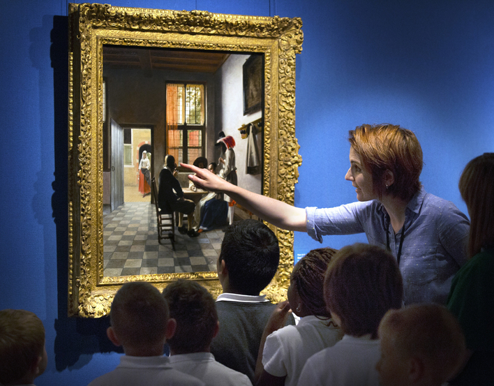 Small group of children with teacher looking closely at a painting on gallery wall