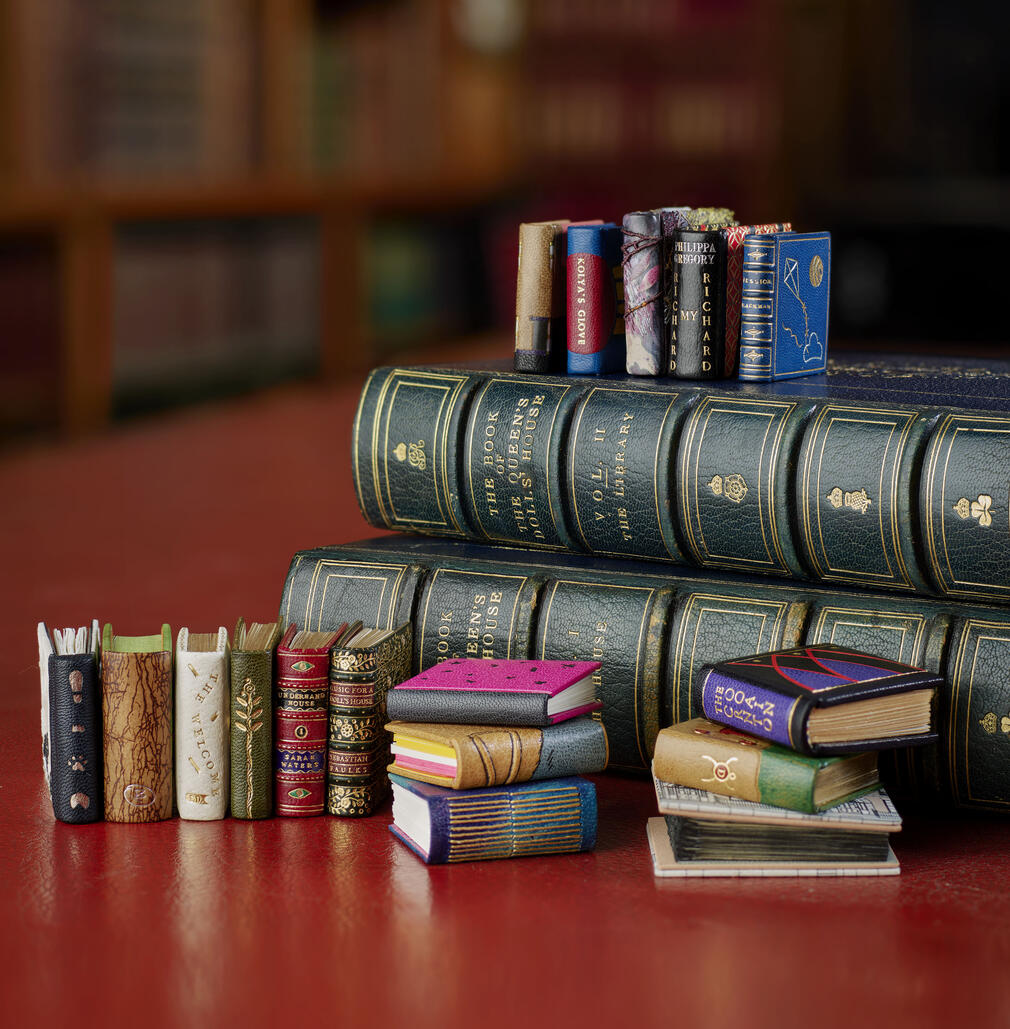 A selection of the new miniature books, with a range of colourful cover designs, shown against the backdrop of the Royal Library at Windsor Castle. 