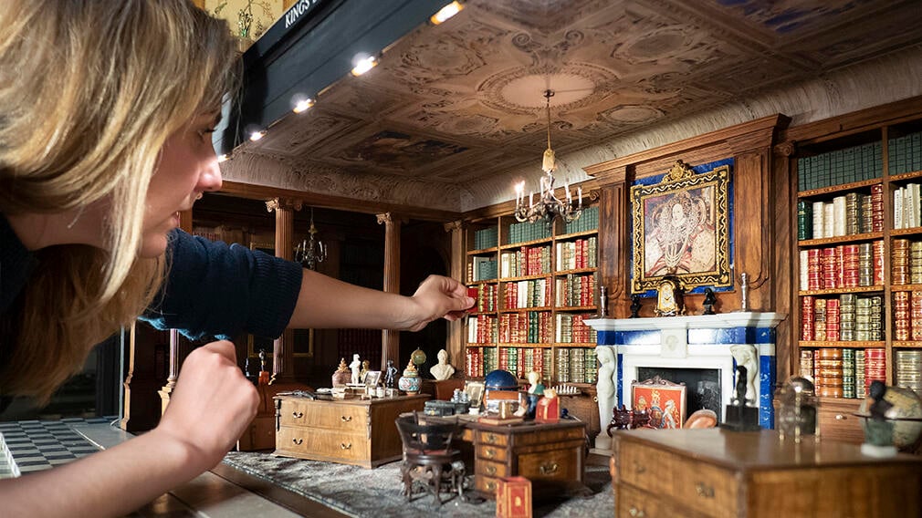 A curator places a miniature book in the Queen Mary's Dolls' House miniature  library