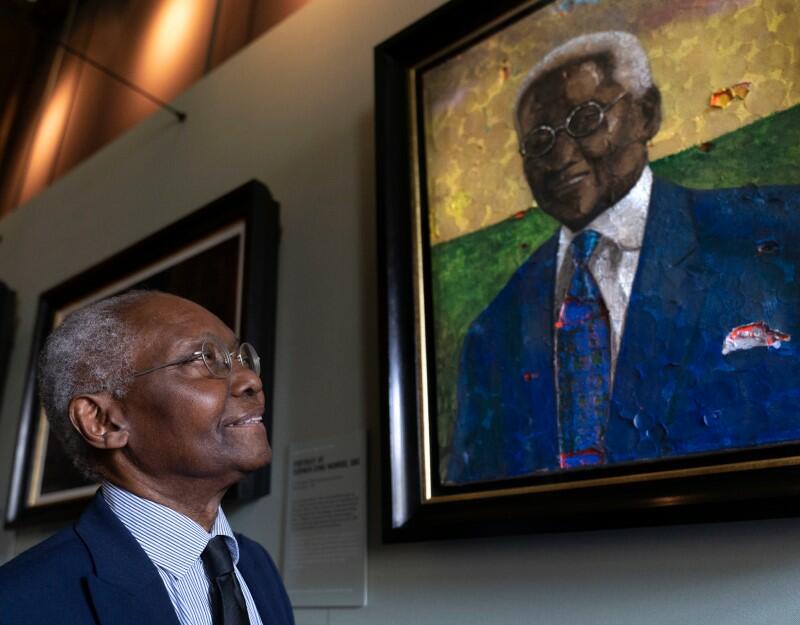 Professor Sir Godfrey (Geoff) Palmer OBE stands next to his portrait painted by Derek Fordjour