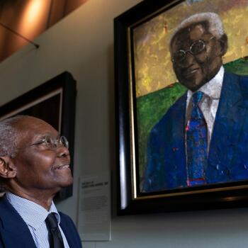 Professor Sir Godfrey (Geoff) Palmer OBE stands next to his portrait painted by Derek Fordjour