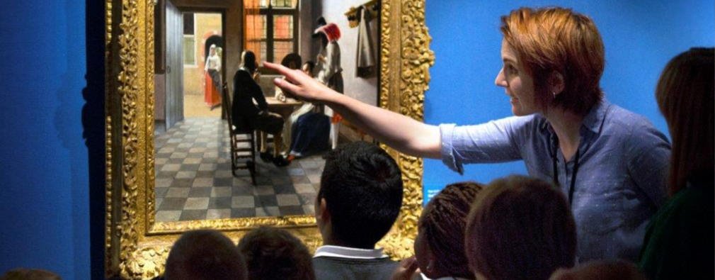 Group of school pupils and teacher looking closely at a painting on a gallery wall