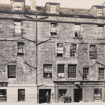 A black and white photo of building in 1903. A man and children stand outside the buildings.